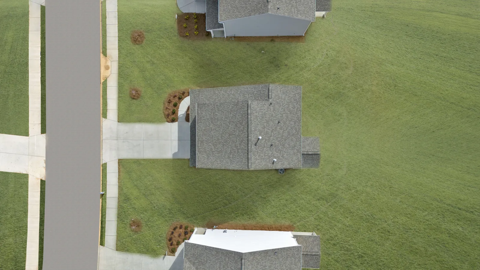 Aerial view of suburban houses with gray roofs, driveways, sidewalks, and green lawns on a clear day