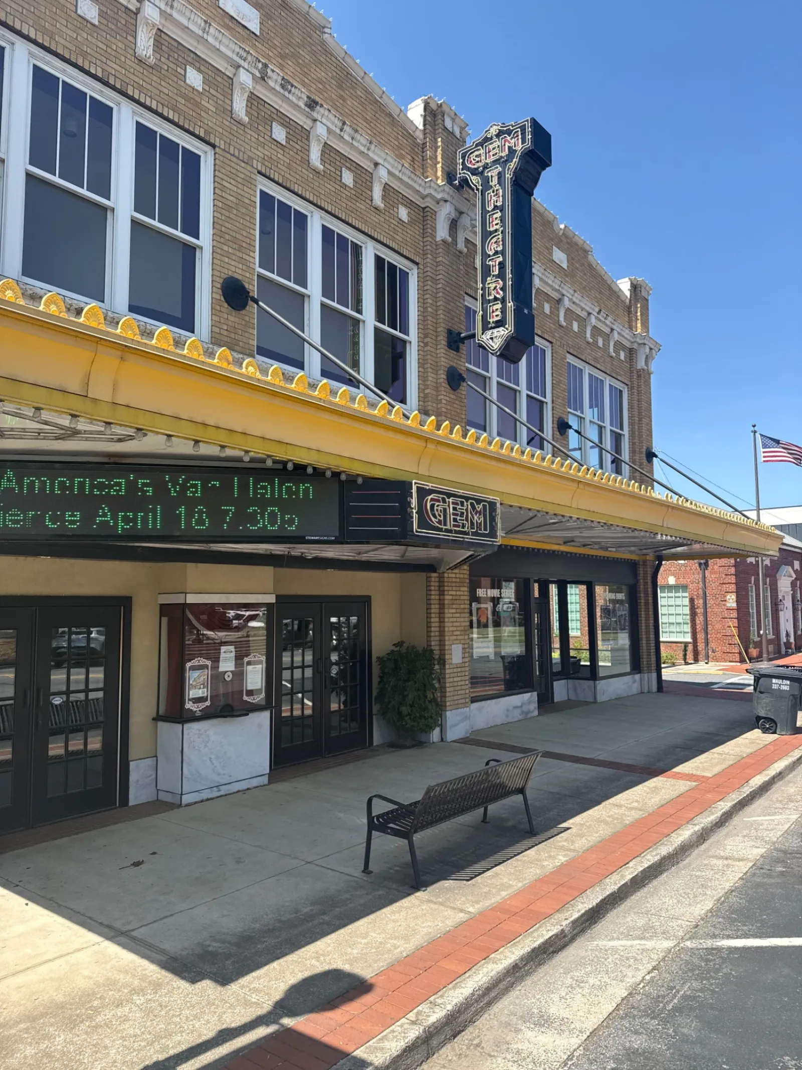 Historic theater building with a yellow marquee and black sign reading 'GEM' on a sunny day.