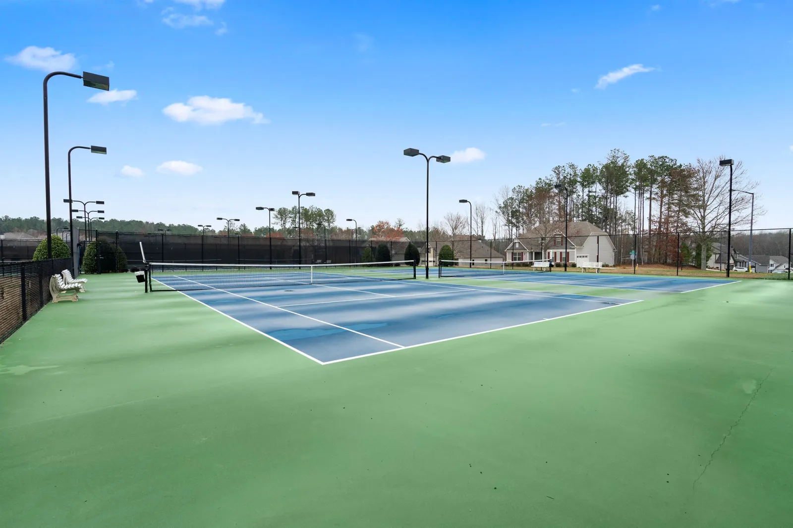 Empty outdoor tennis courts with blue and green surfaces under a clear blue sky and surrounding trees.