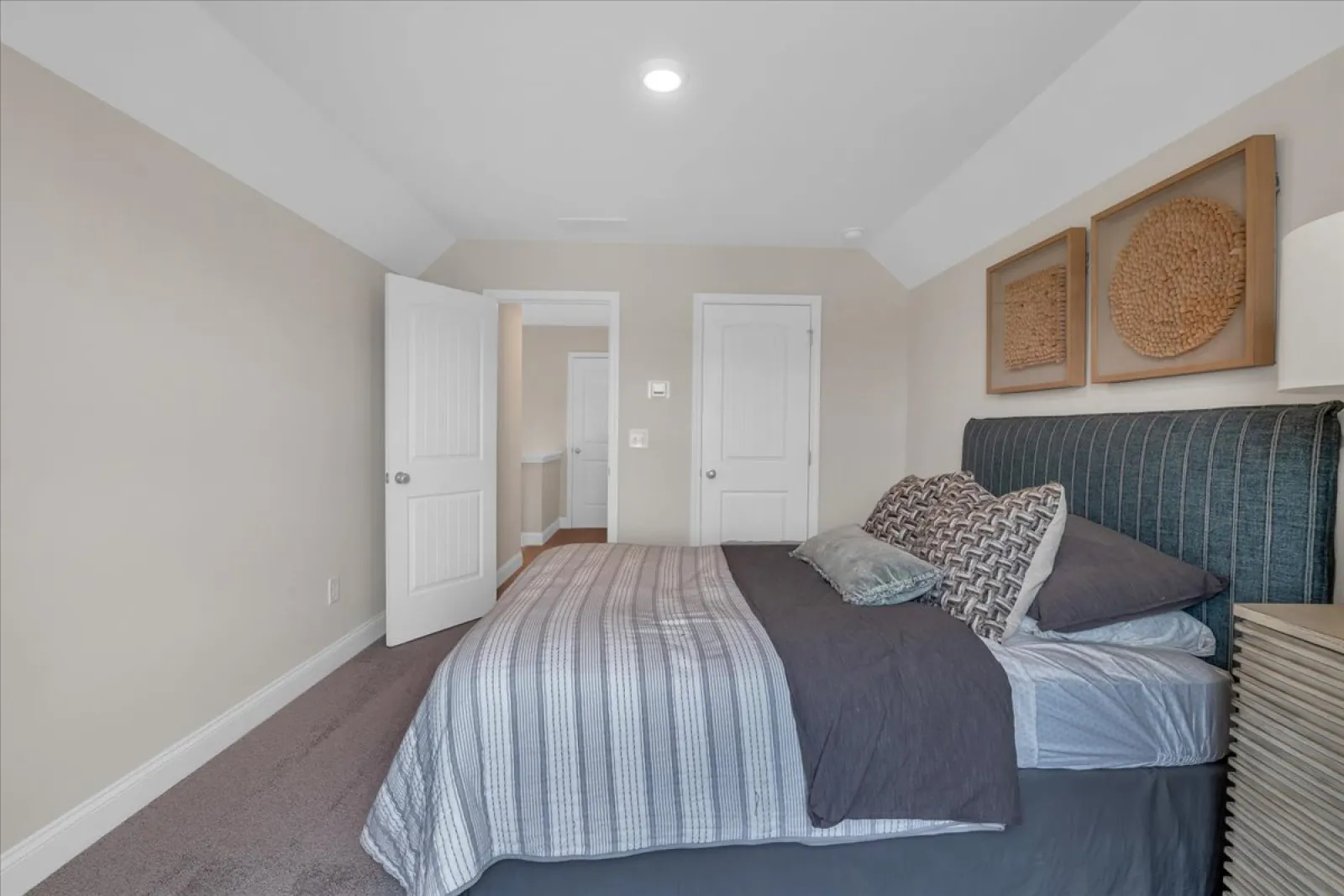 Minimalist bedroom with gray striped bedding, upholstered headboard, decorative wall art, and neutral walls.