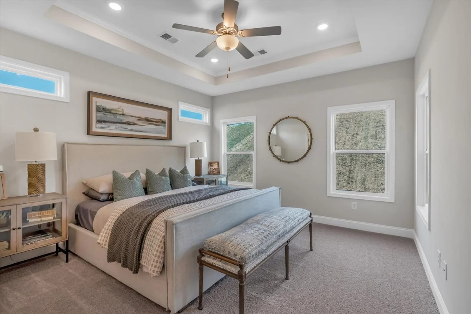 Modern bedroom with plush bed, patterned bench, ceiling fan, two windows, and minimalistic decor in soft tones
