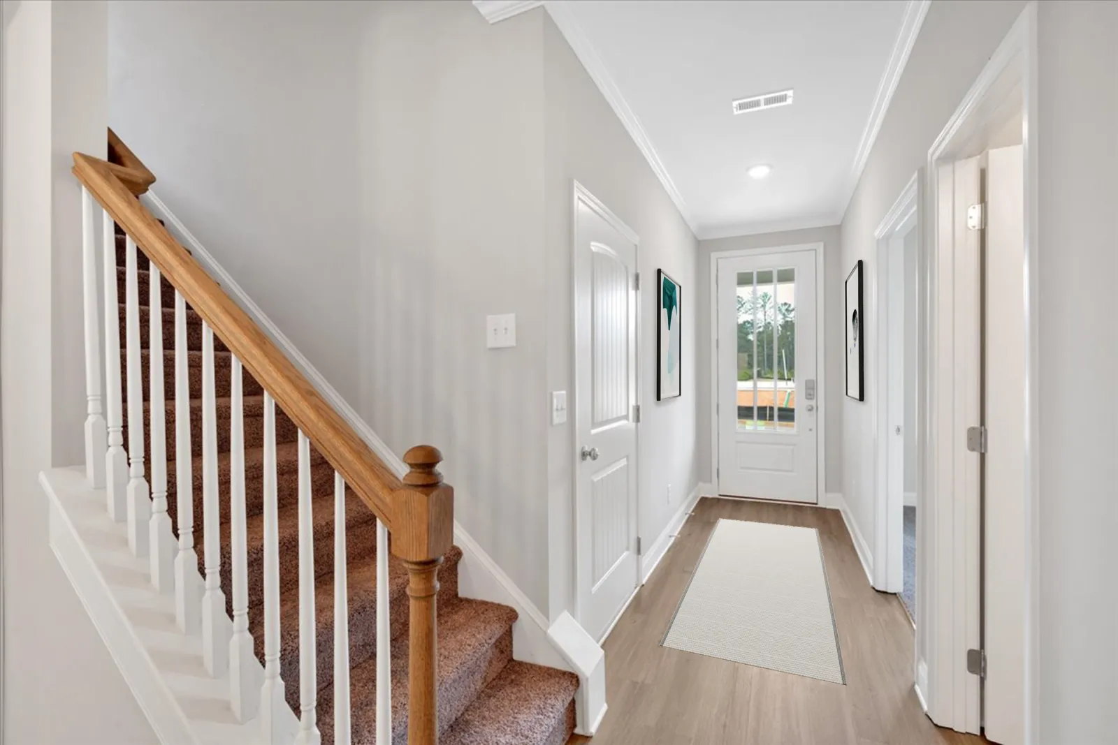 Bright hallway with beige rug, white doors, gray walls, and carpeted wooden staircase with white spindles.