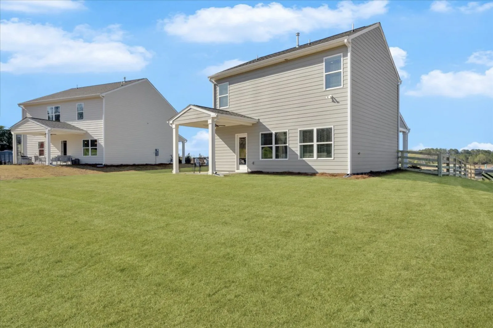 Two modern houses with spacious yards under a blue sky, showcasing a suburban landscape.