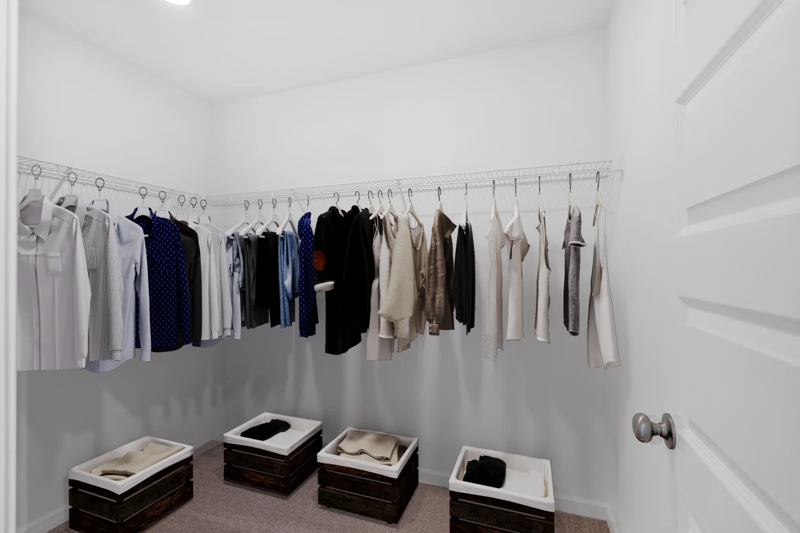 Organized walk-in closet with hanging shirts, sweaters, and storage bins on carpeted floor under bright lighting