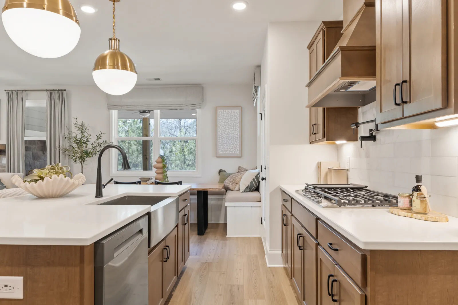 Modern kitchen with wood cabinets, white countertops, farmhouse sink, pendant lights, and a cozy breakfast nook.