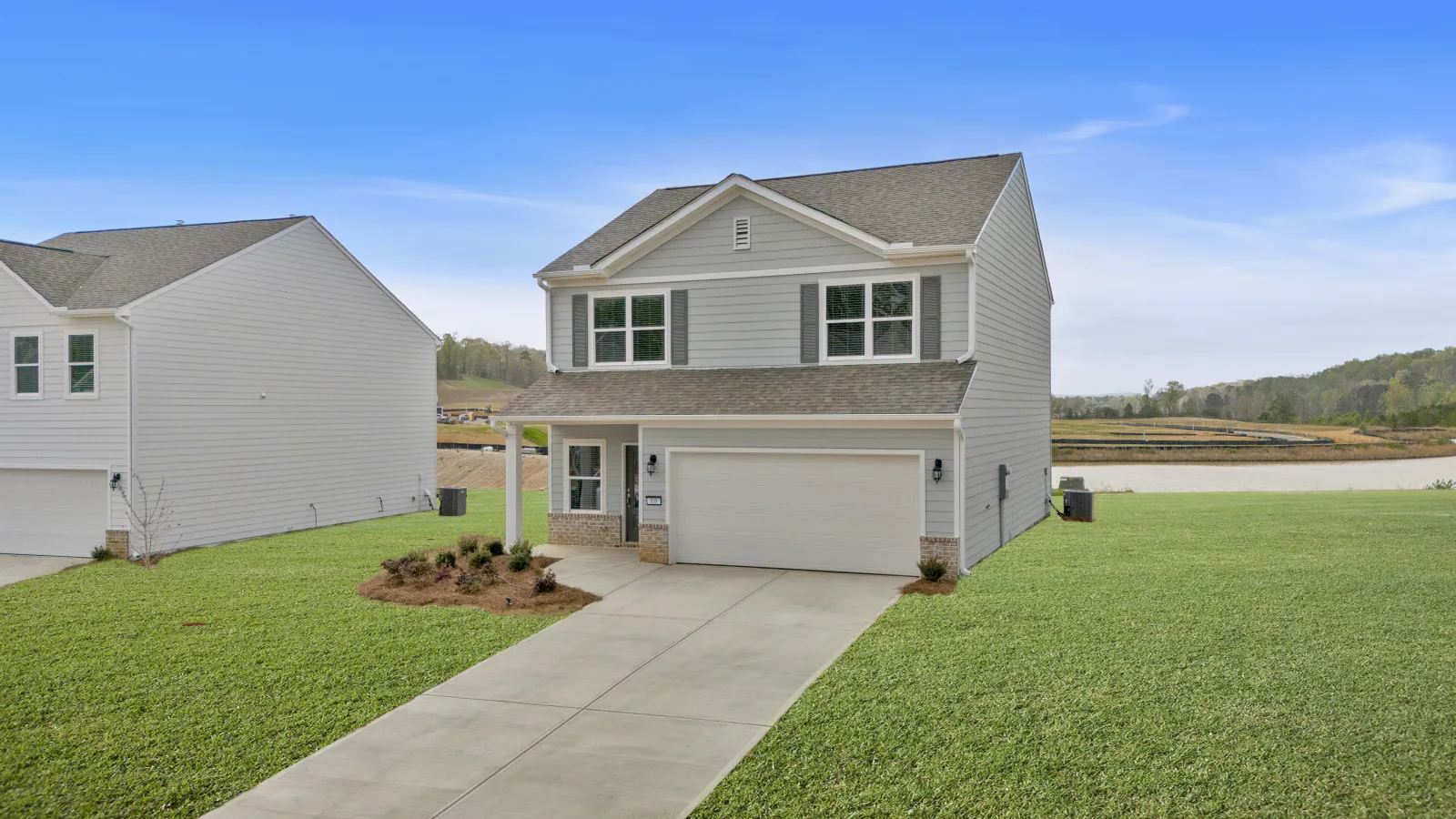 Two-story white suburban house with a double garage, concrete driveway, and green lawn under a blue sky.