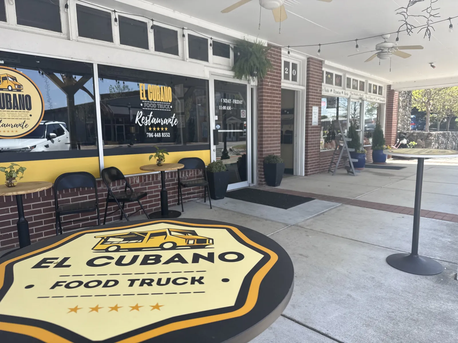 Outdoor seating area and entrance of El Cubano Food Truck restaurante with branded tables and brick walls.