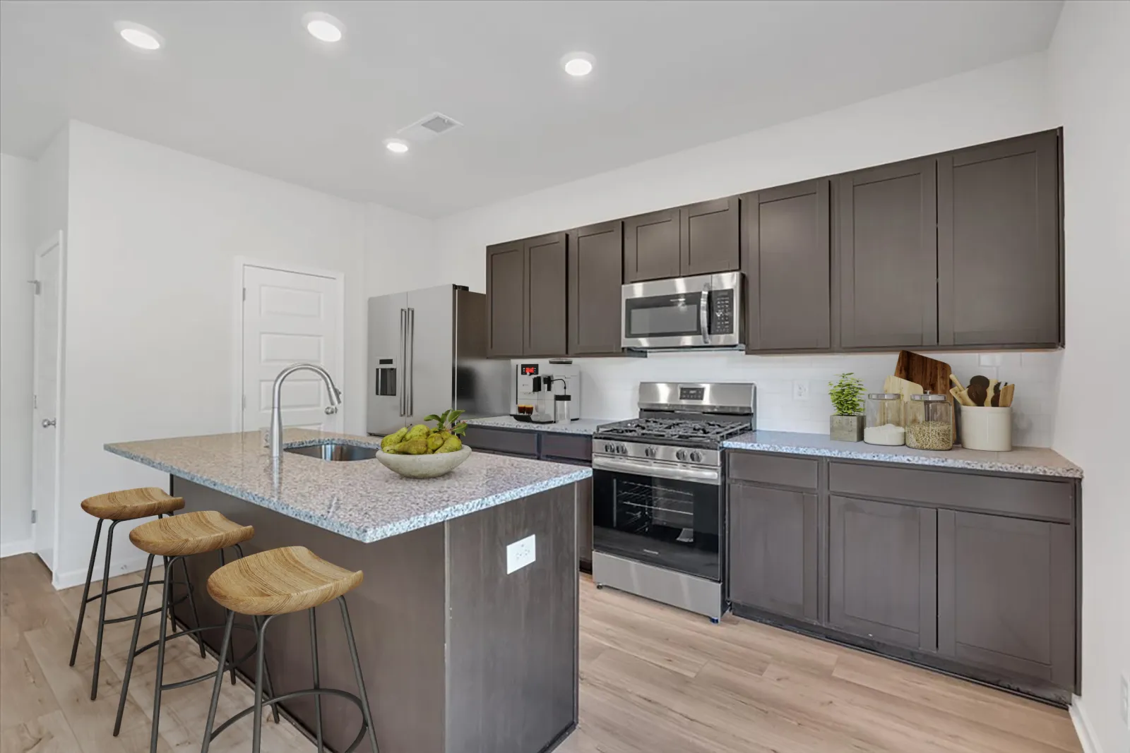 Modern kitchen with dark cabinets, granite countertops, stainless steel appliances, and wooden bar stools.