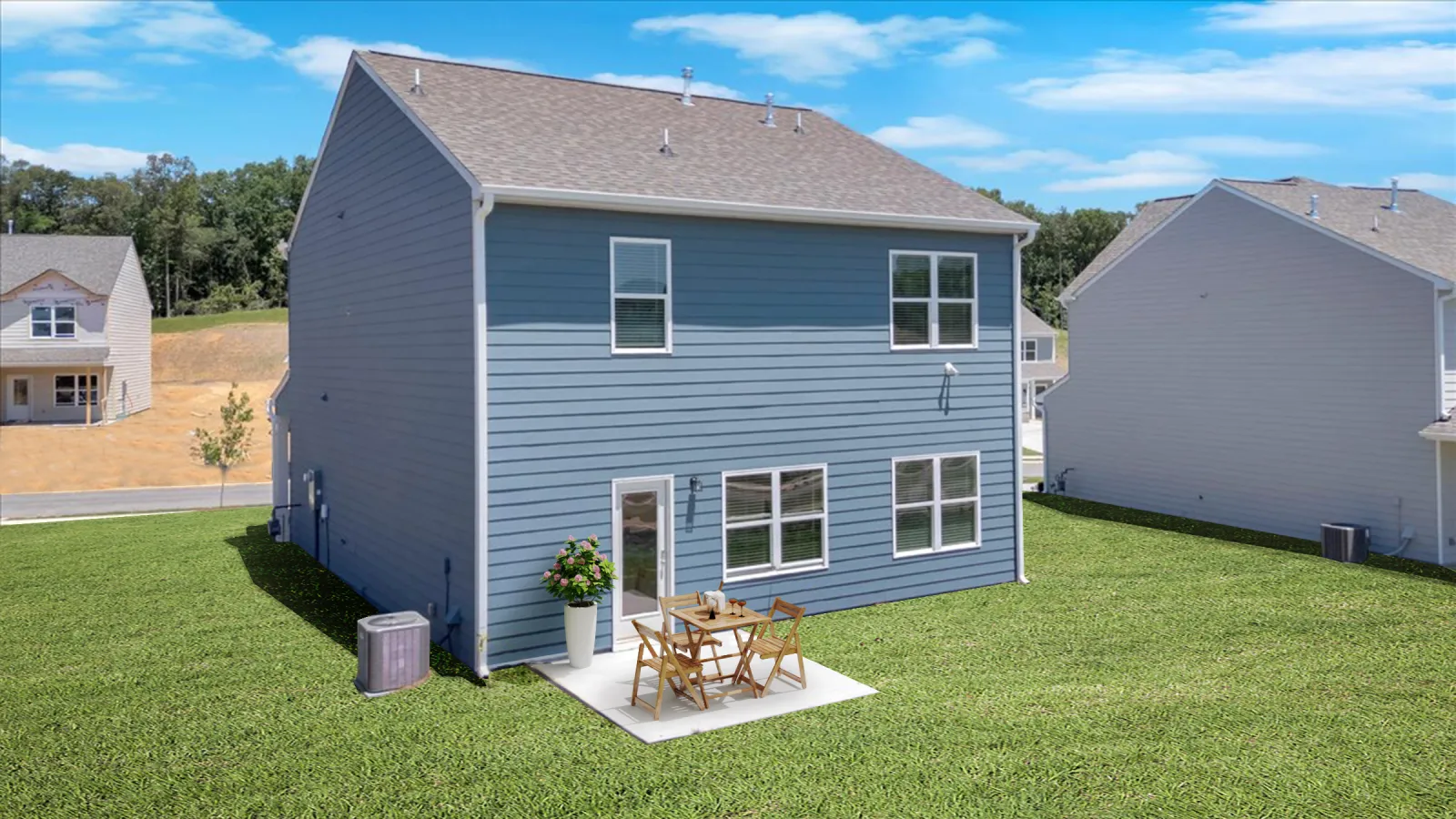 Blue two-story house with a small patio and outdoor furniture on a green lawn under blue sky