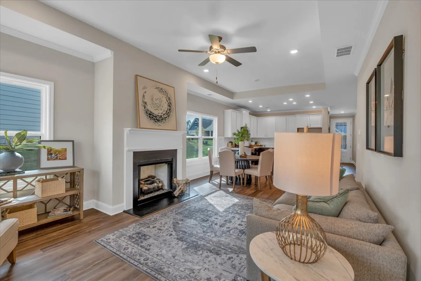 Bright, open living room and dining area with fireplace, ceiling fan, modern furniture, and hardwood floors.