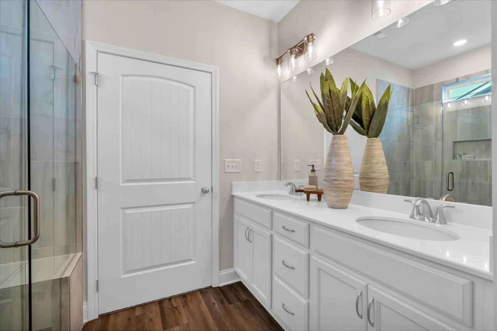 Modern bathroom with double sink white vanity, large mirror, glass shower, and wooden floor