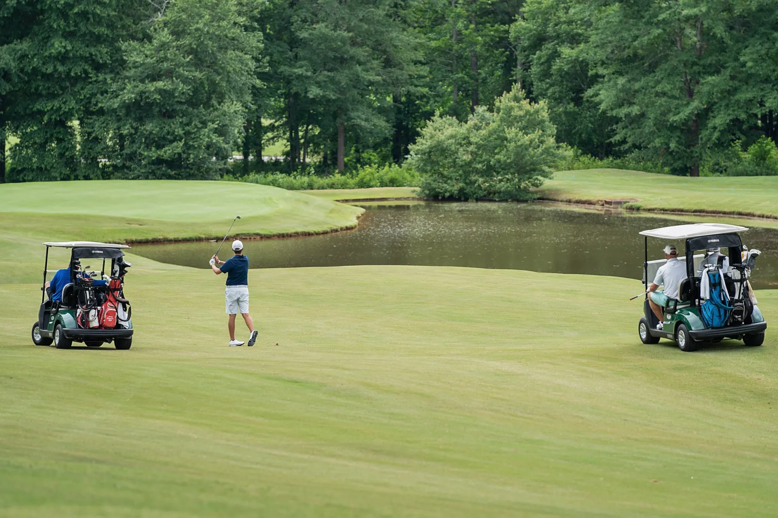 people on golf carts watching another person hit a ball on the golf course