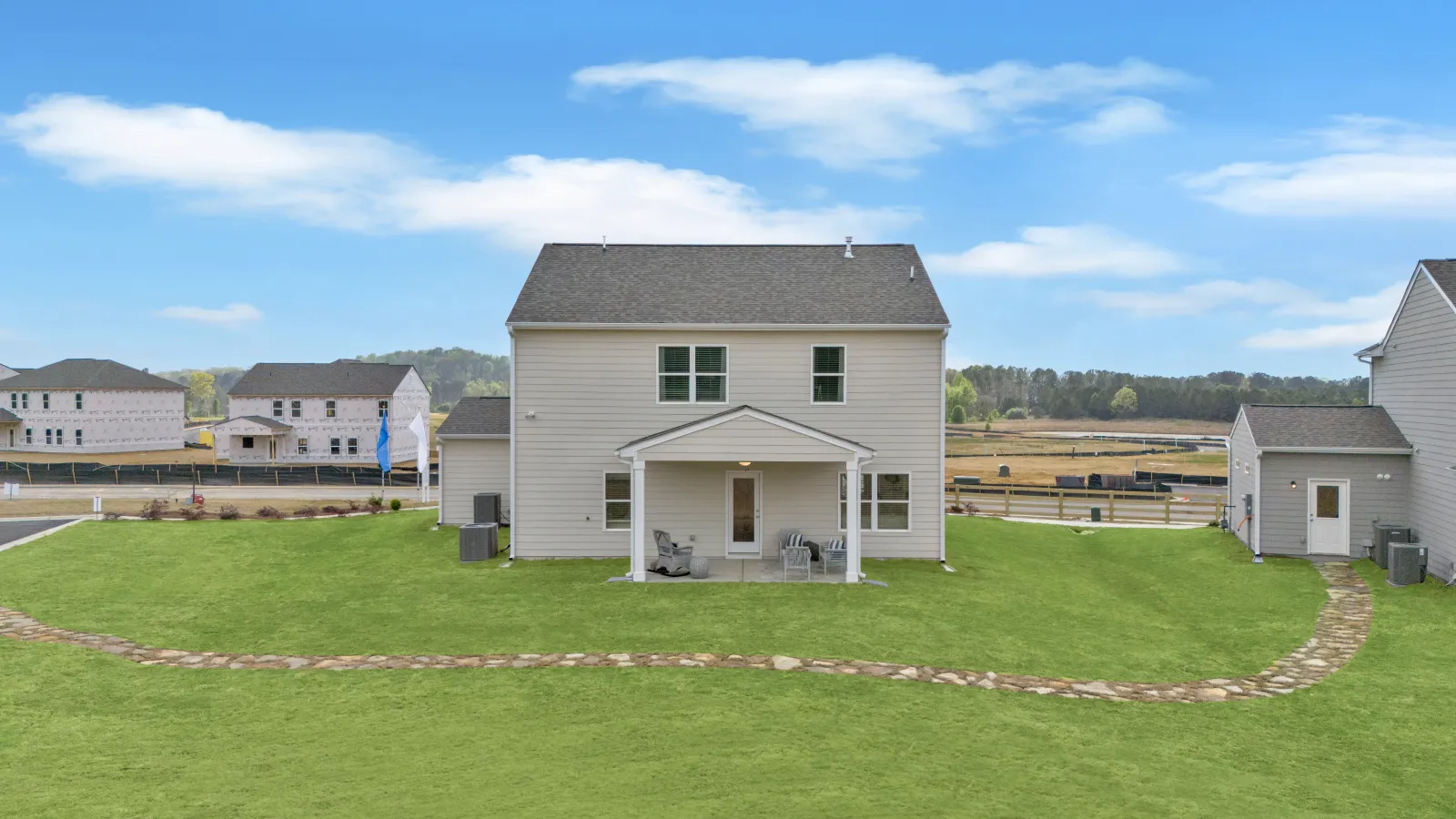 Rear view of a modern house with green lawn and clear blue sky, showcasing outdoor living space.