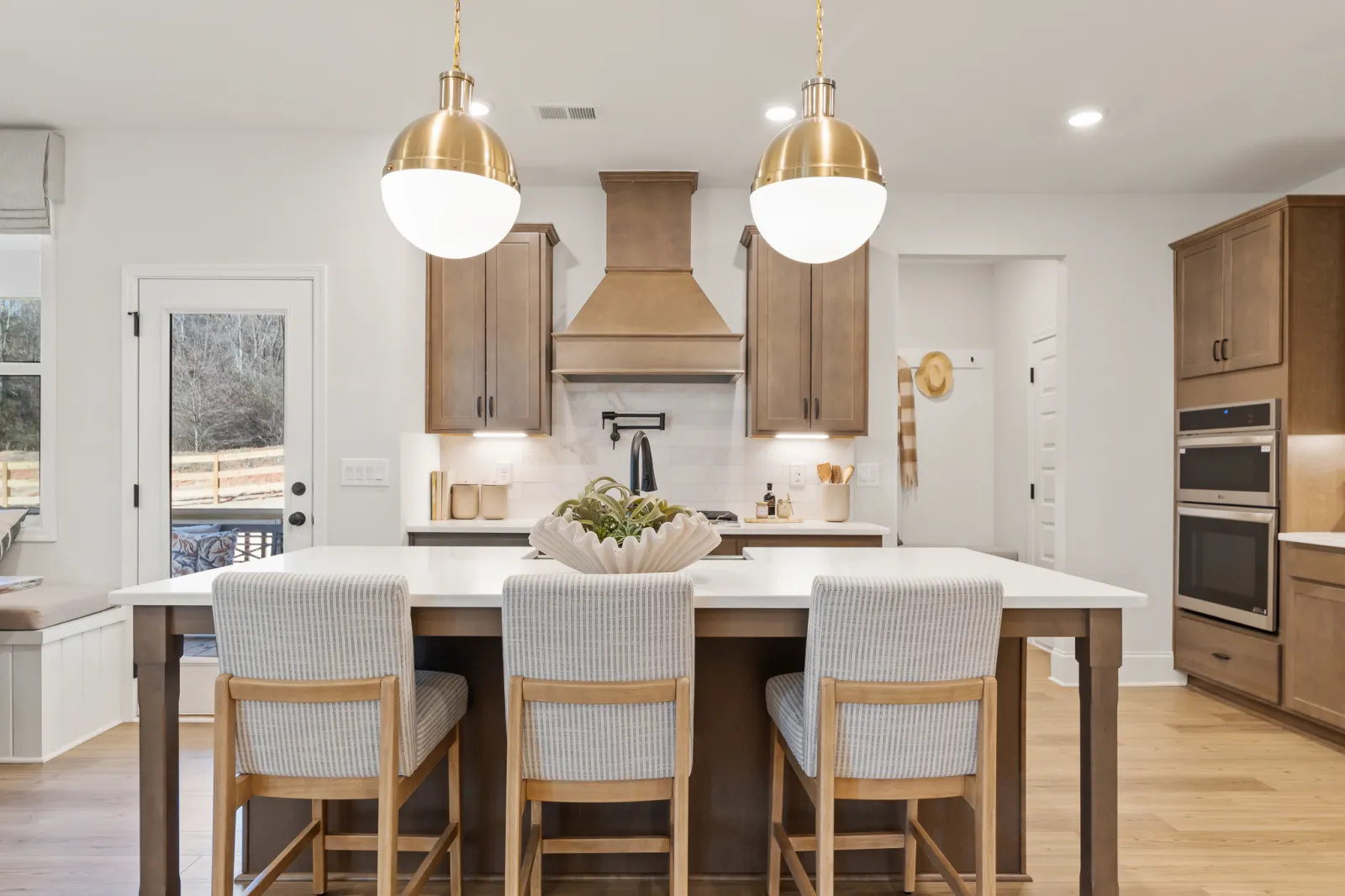 Modern kitchen with wooden cabinets, white countertops, three cushioned chairs, and brass pendant lights
