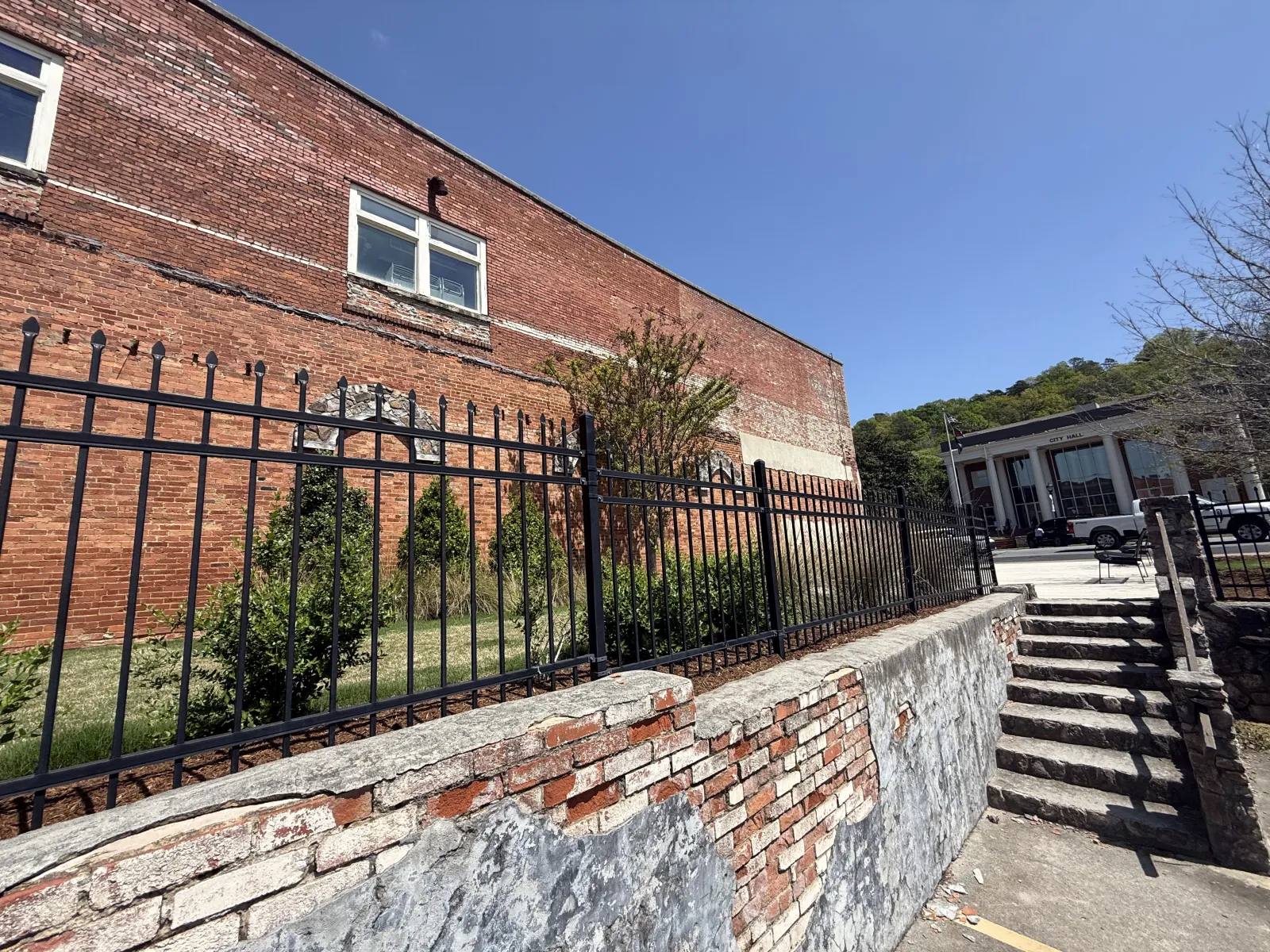 Black metal fence along old brick building with stone stairs under clear blue sky on sunny day