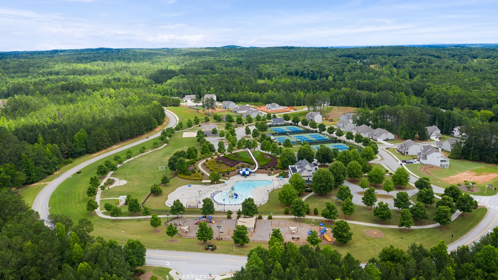 Aerial view of a suburban park with a water playground, tennis courts, walking paths, and surrounding houses.