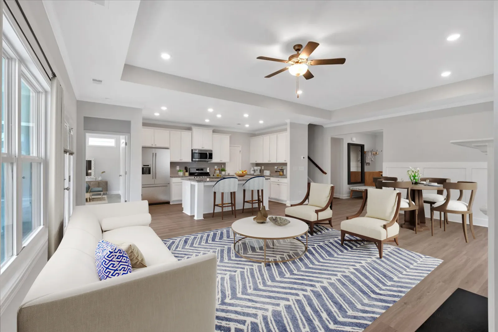 Open floor plan living room with white sofa, blue patterned rug, wooden chairs, modern kitchen, and dining area.