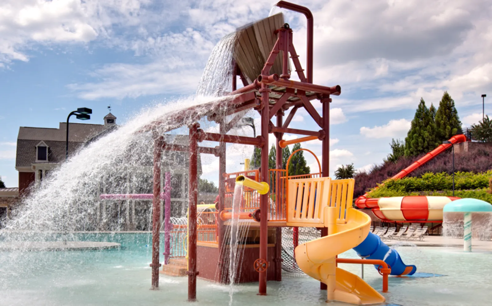 Colorful water playground with slides and large tipping bucket pouring water into a shallow pool under blue sky.