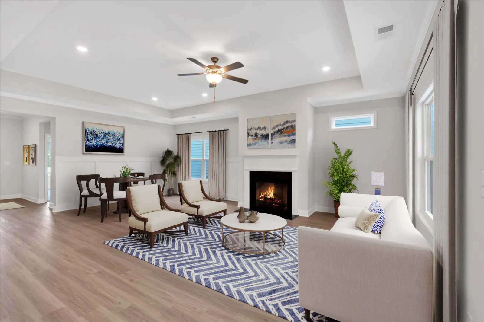 Spacious modern living room with fireplace, white sofa, two armchairs, blue patterned rug, and dining area in background.
