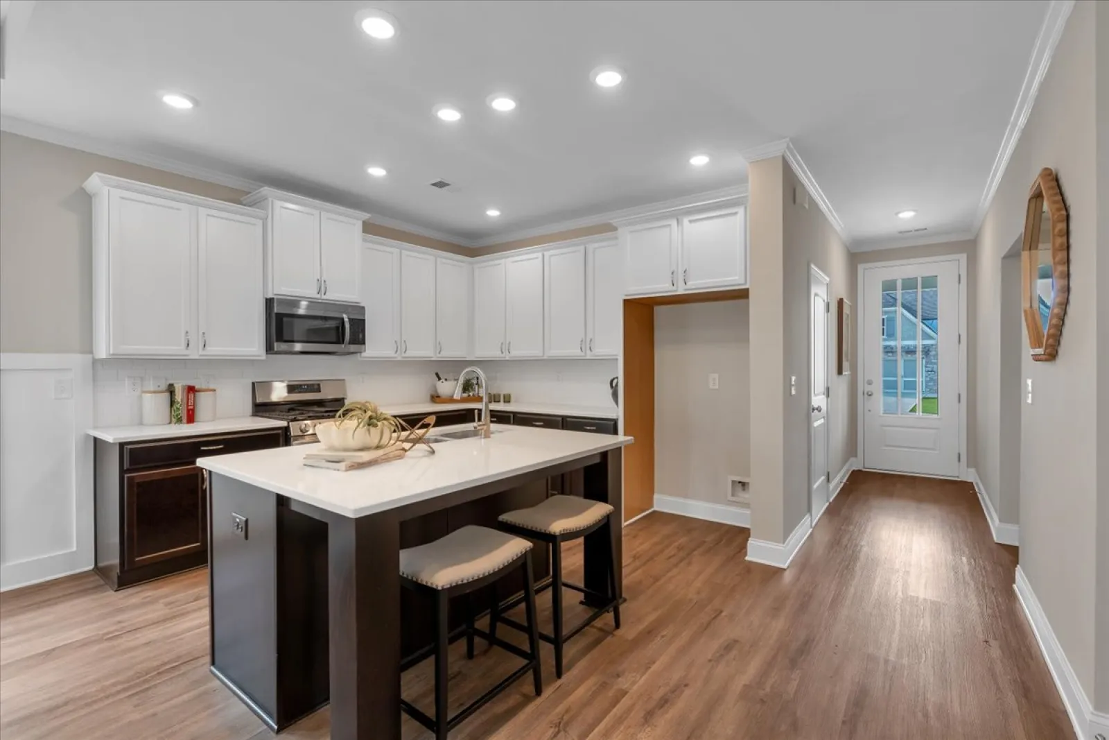 Modern kitchen with white cabinets, black island with stools, stainless steel appliances, and wood flooring.