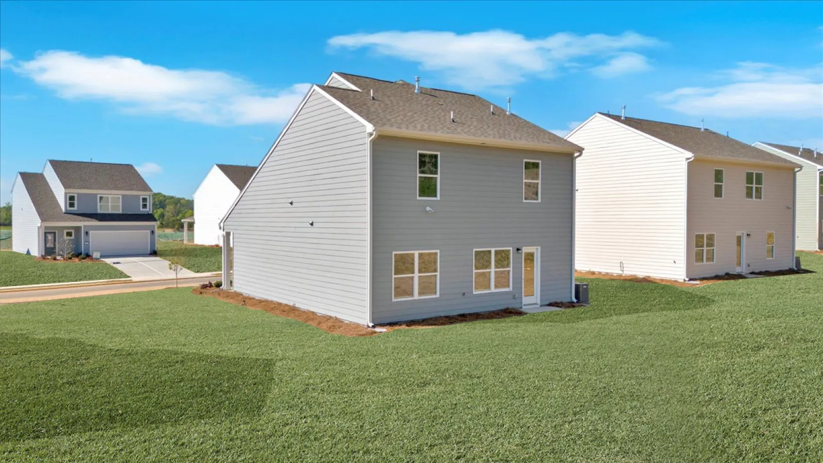 Suburban neighborhood with modern two-story houses and green lawns under a blue sky with clouds.