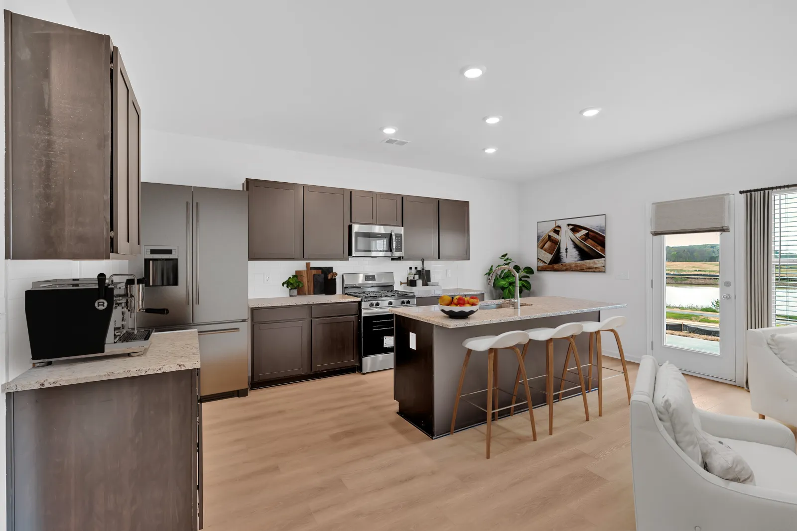 Modern kitchen with dark cabinets, stainless steel appliances, large island with stools, and light wood floors.