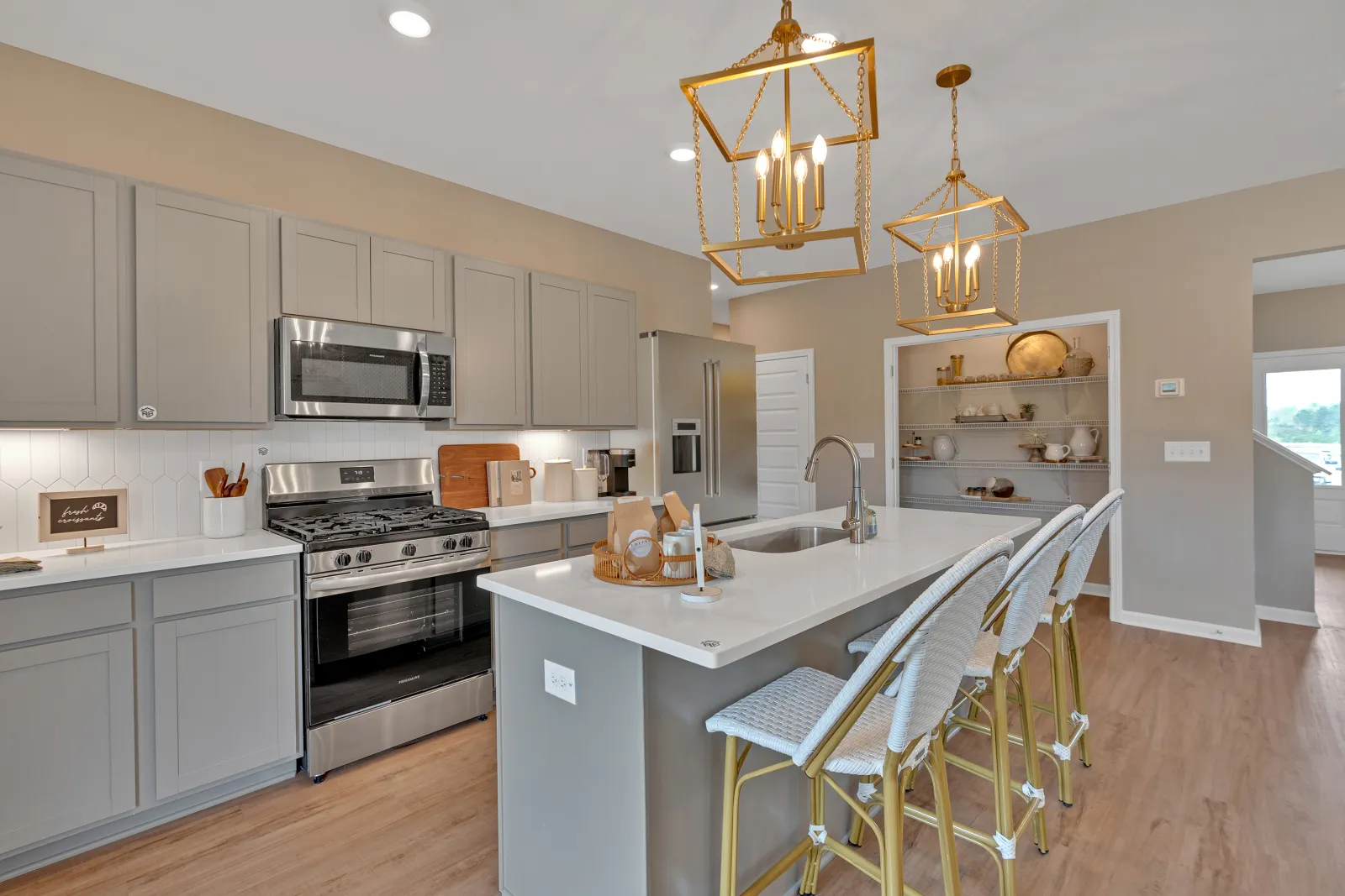 Modern kitchen featuring gray cabinets, white countertops, and stylish golden pendant lights.