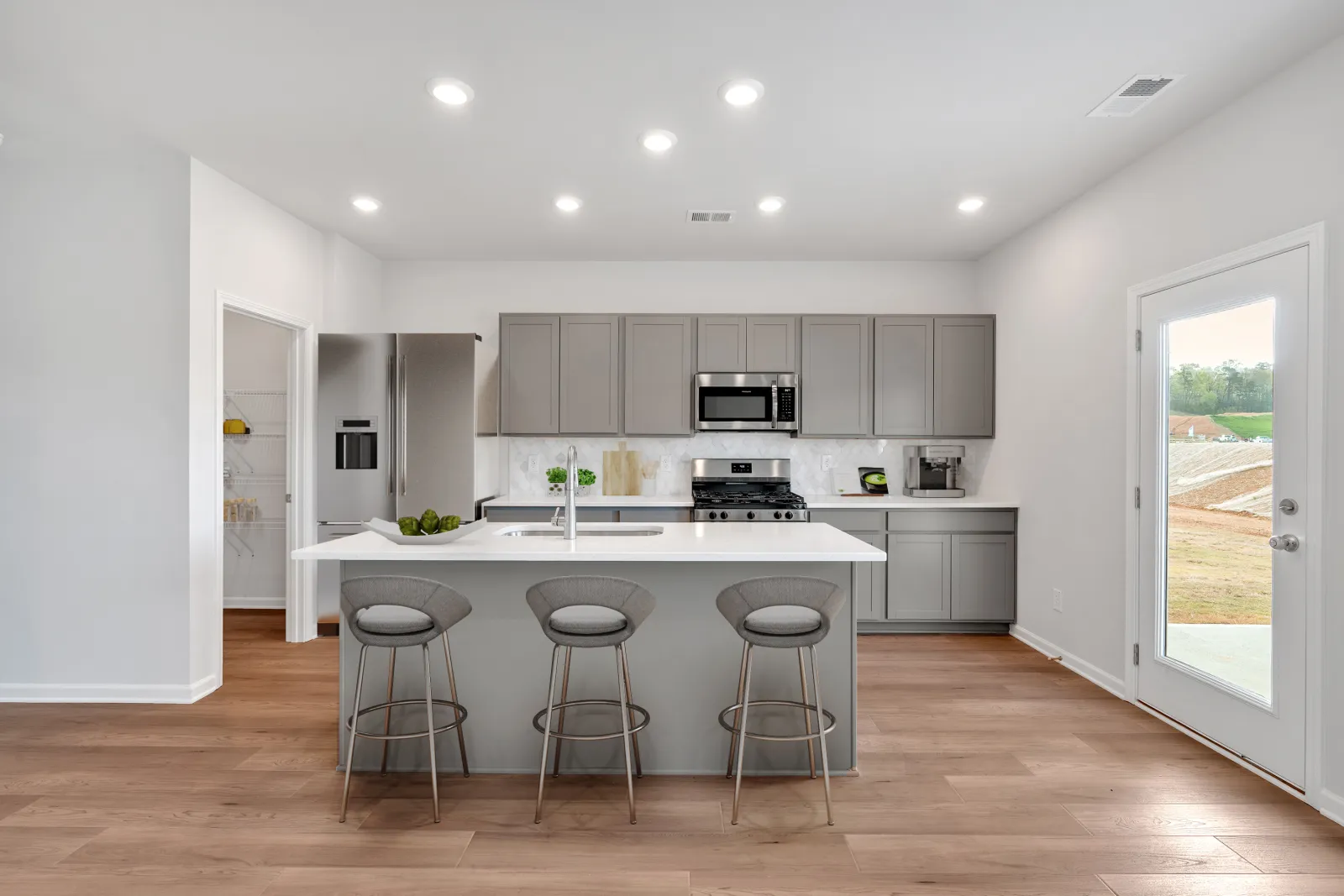 Modern kitchen with gray cabinets, stainless steel appliances, island with three stools, and wood flooring