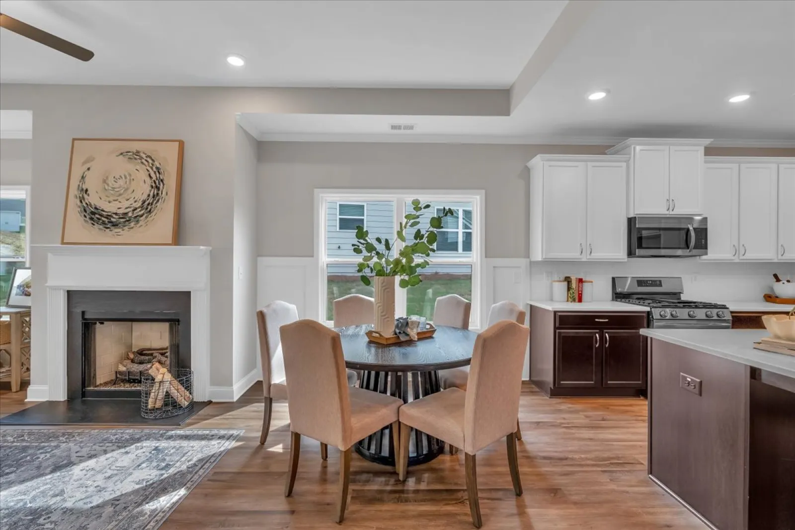 Modern dining area with a round table, beige chairs, fireplace, and white kitchen cabinets in an open floor plan.