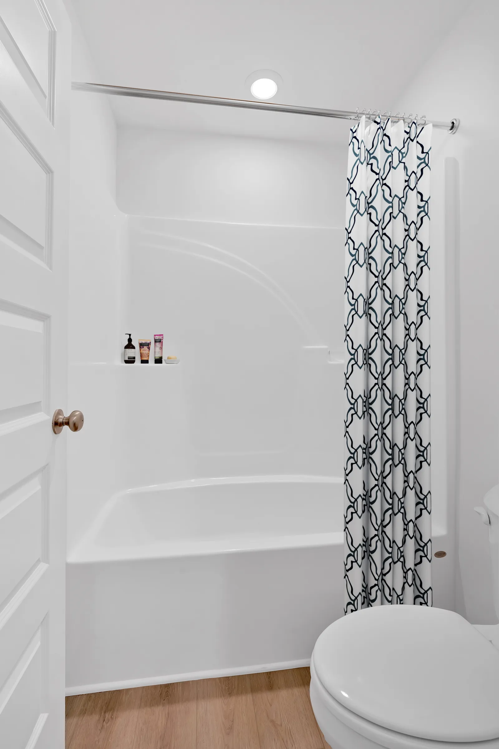 Minimalist white bathroom featuring a bathtub with patterned curtain and wooden floor.