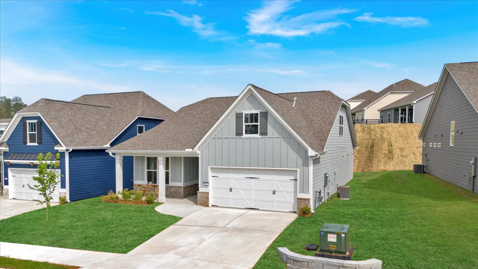 Modern suburban homes with green lawns, driveways, and clear blue sky in a residential neighborhood.