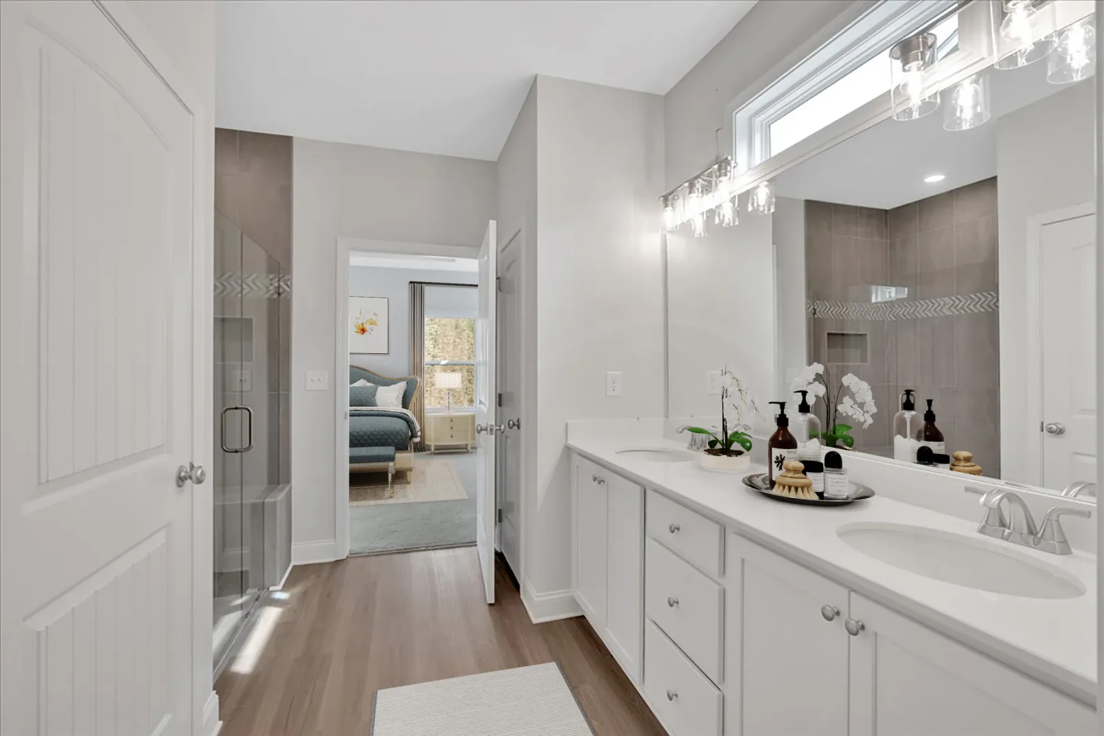 Modern bathroom with double vanity, large mirror, glass shower, and view into adjacent bedroom