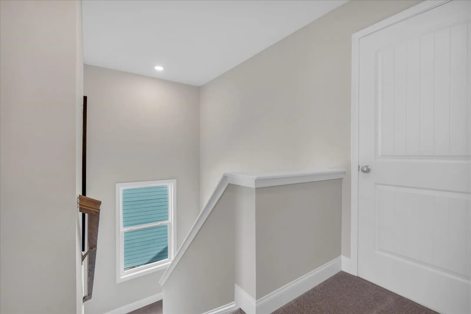 Bright landing area at top of stairs with beige walls, white trim, and closed white door.