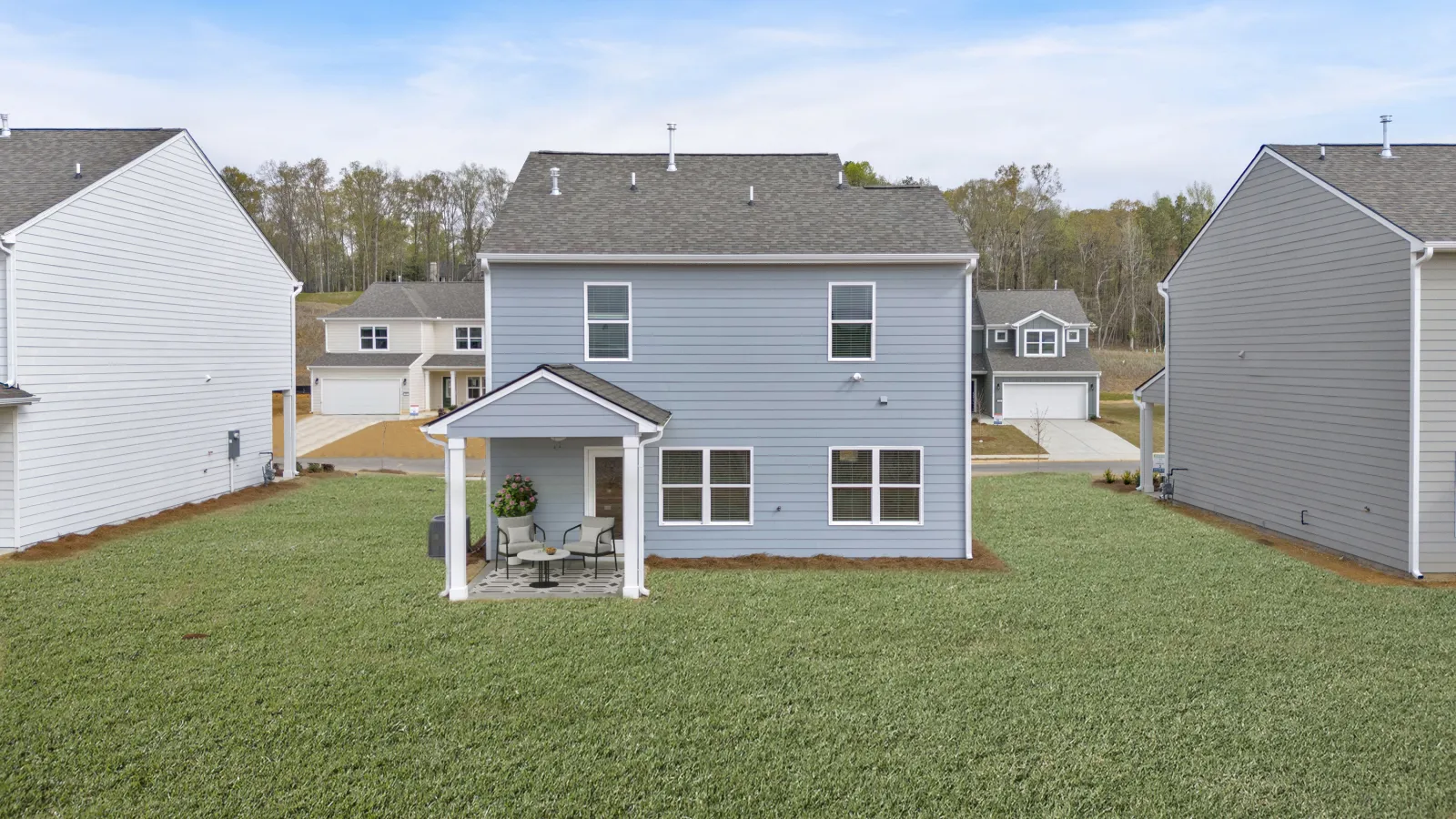 Modern two-story house with a porch in a suburban neighborhood surrounded by green grass.