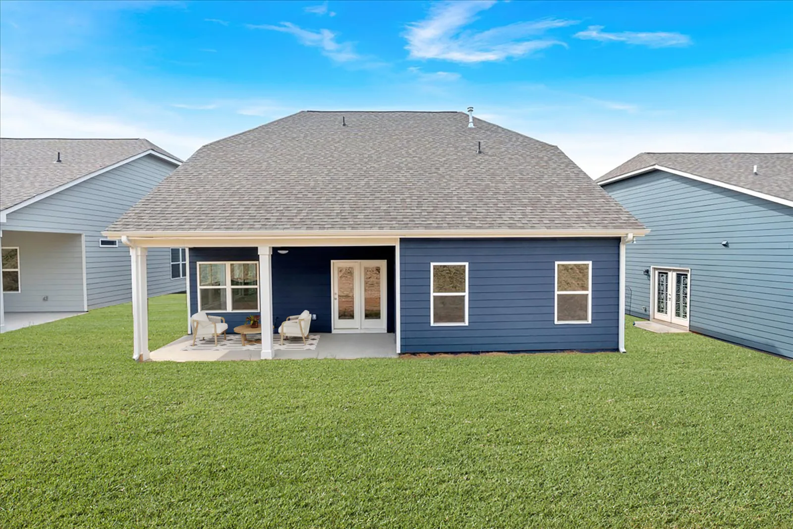 Modern blue house with covered patio and outdoor seating on a large green lawn under a clear sky