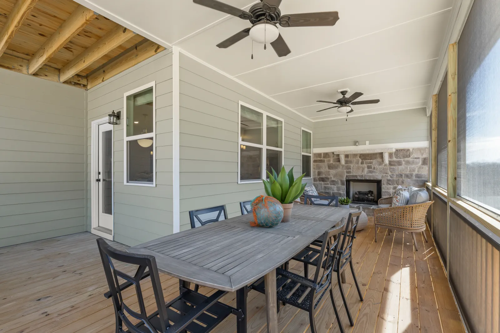 Spacious screened porch with wooden flooring, dining table, chairs, ceiling fans, and stone fireplace.