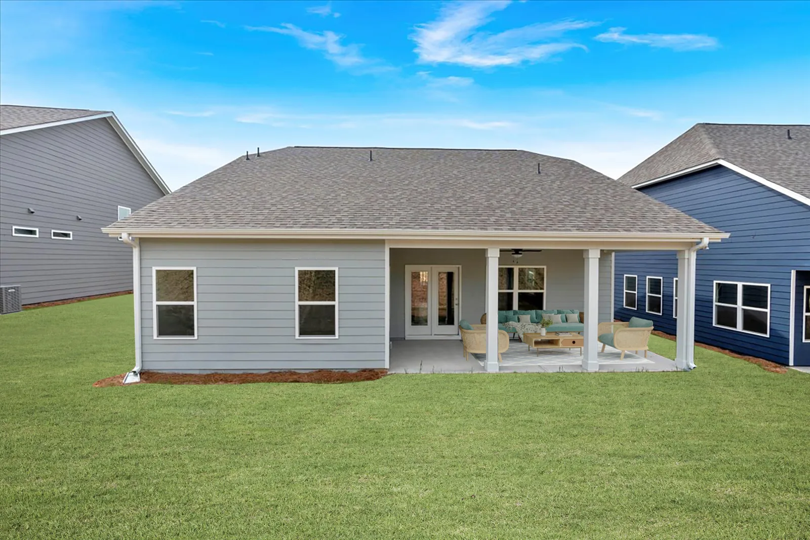 Modern gray single-story house with covered patio and outdoor seating in a green lawn backyard.