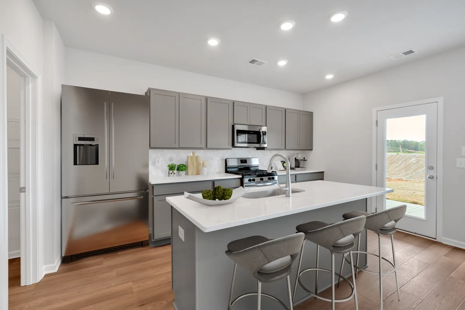 Modern kitchen with gray cabinets, stainless steel appliances, white island countertop, and bar stools under recessed lighting