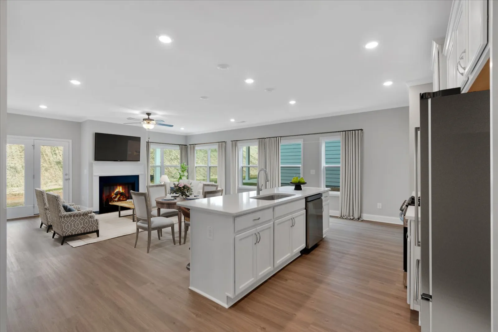 Open concept kitchen and living room with white cabinets, hardwood floors, fireplace, and large windows.