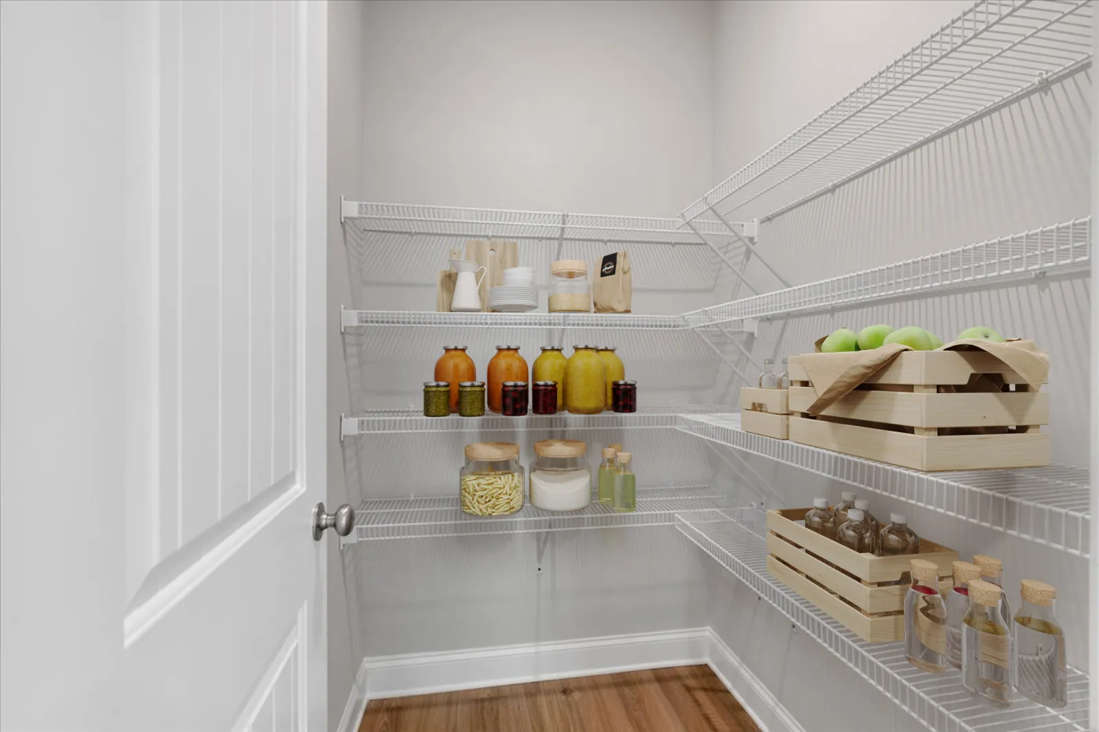 Organized pantry with wire shelves holding jars, bottles, wooden crates with green apples, and dry goods.