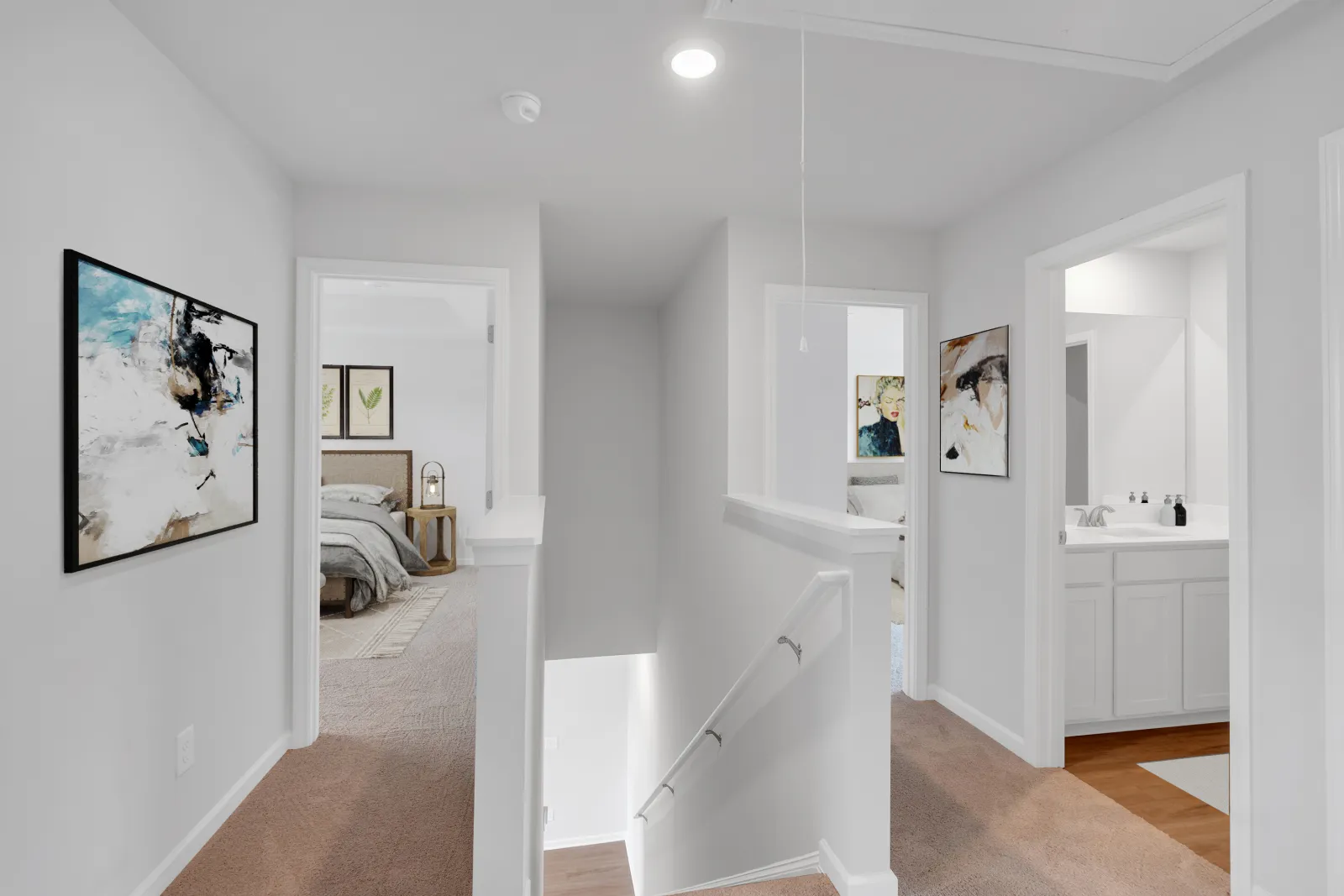Bright hallway with carpeted floors, leading to bedrooms and a bathroom with modern decor and framed artwork.