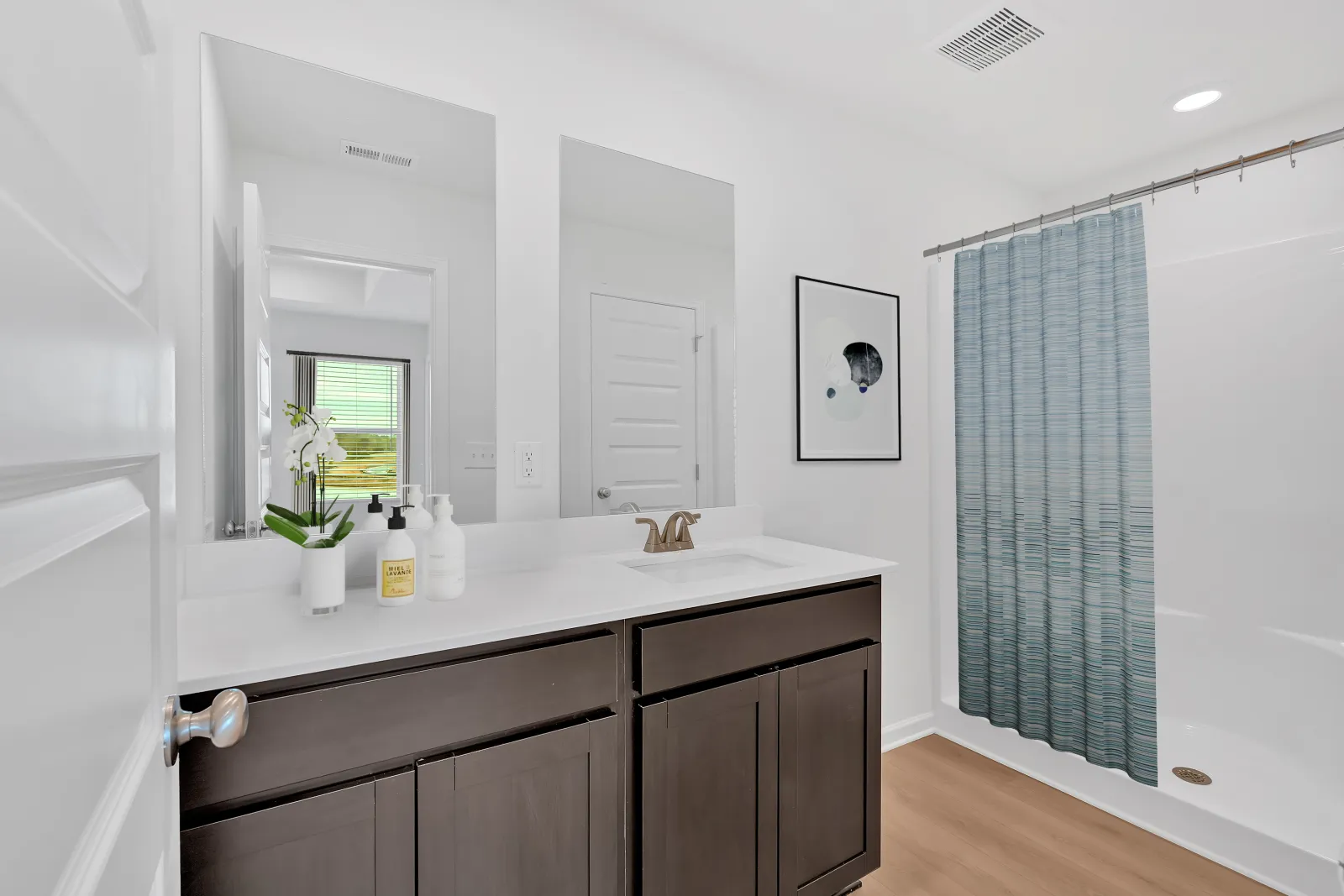 Modern bathroom with dark wood vanity, white countertop, dual mirrors, and blue shower curtain on wooden floor