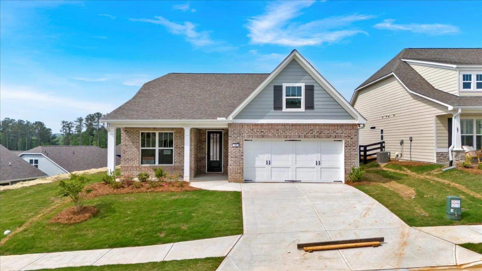 Modern single-story brick house with a two-car garage and a green lawn under a bright blue sky