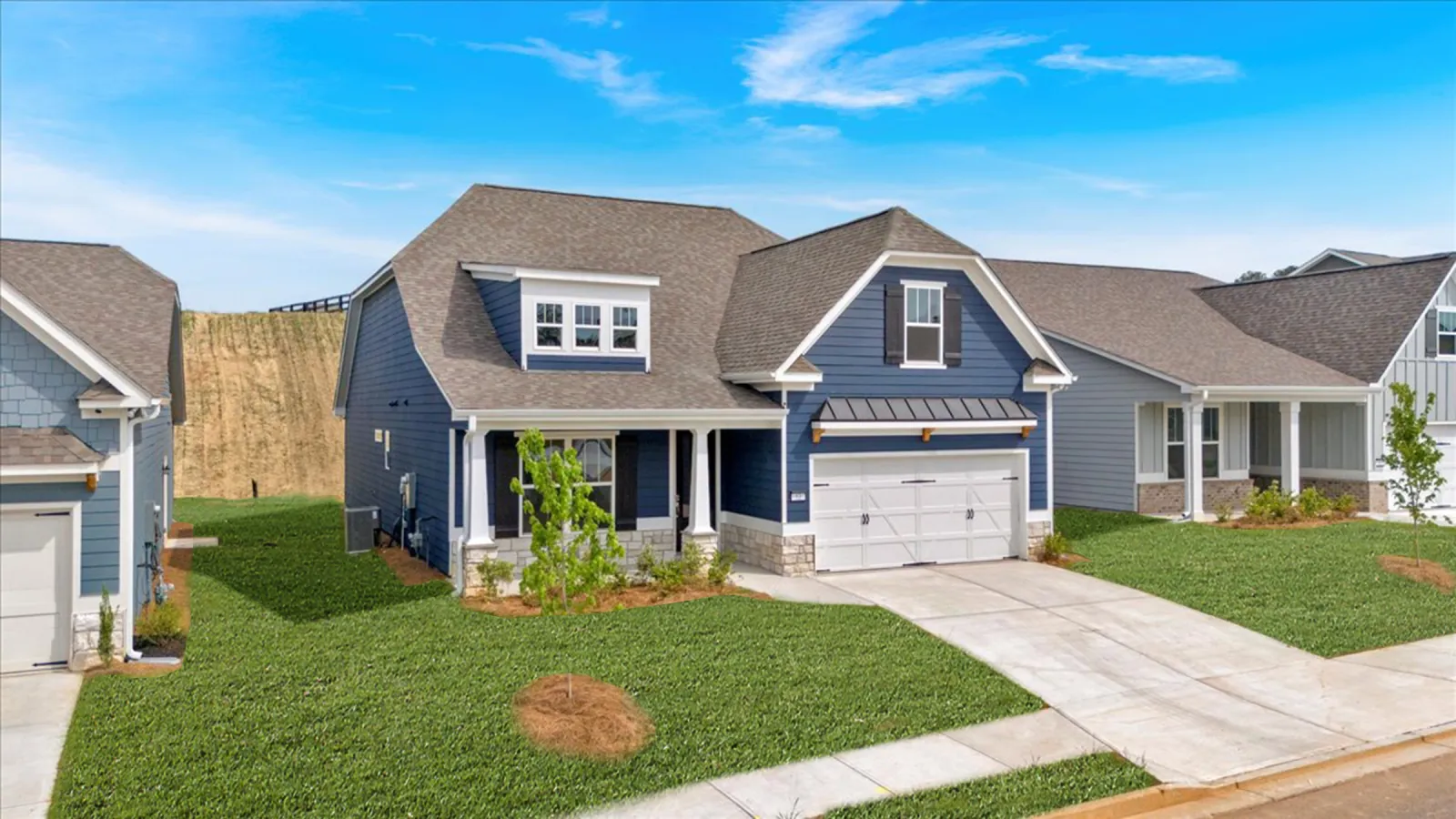 Modern blue and gray suburban homes with manicured lawns under a clear blue sky on a sunny day