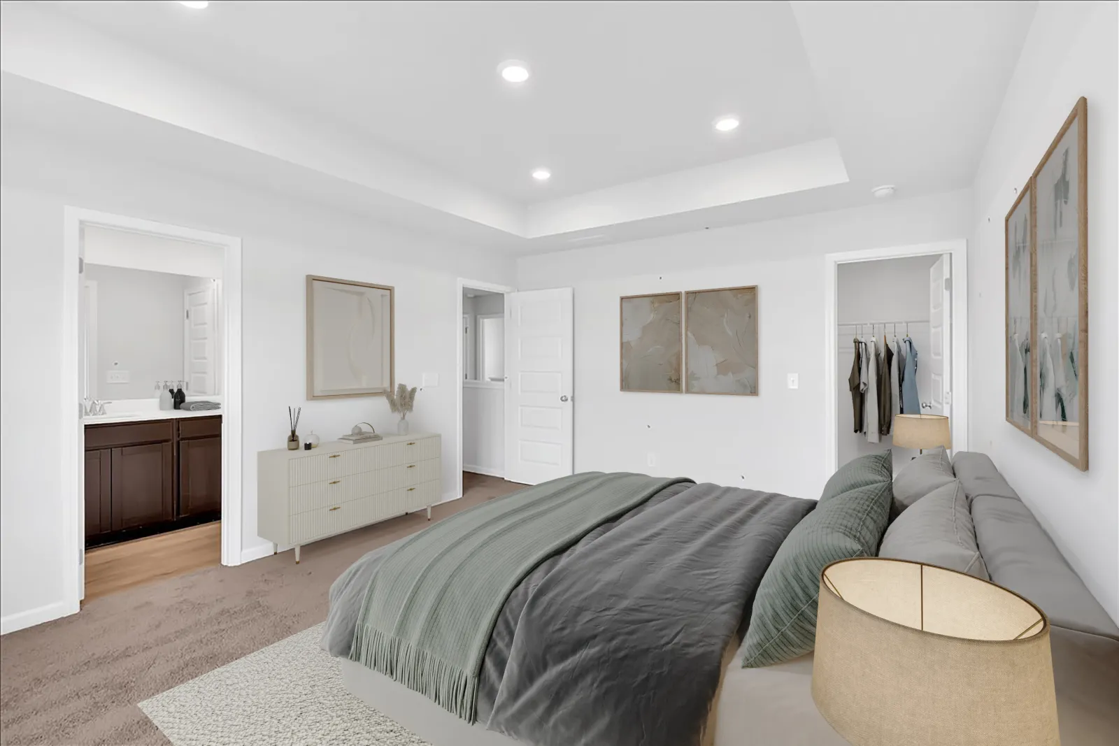 Modern bedroom with gray bedding, white walls, carpet flooring, dresser, framed art, and open doors to bathroom and closet.