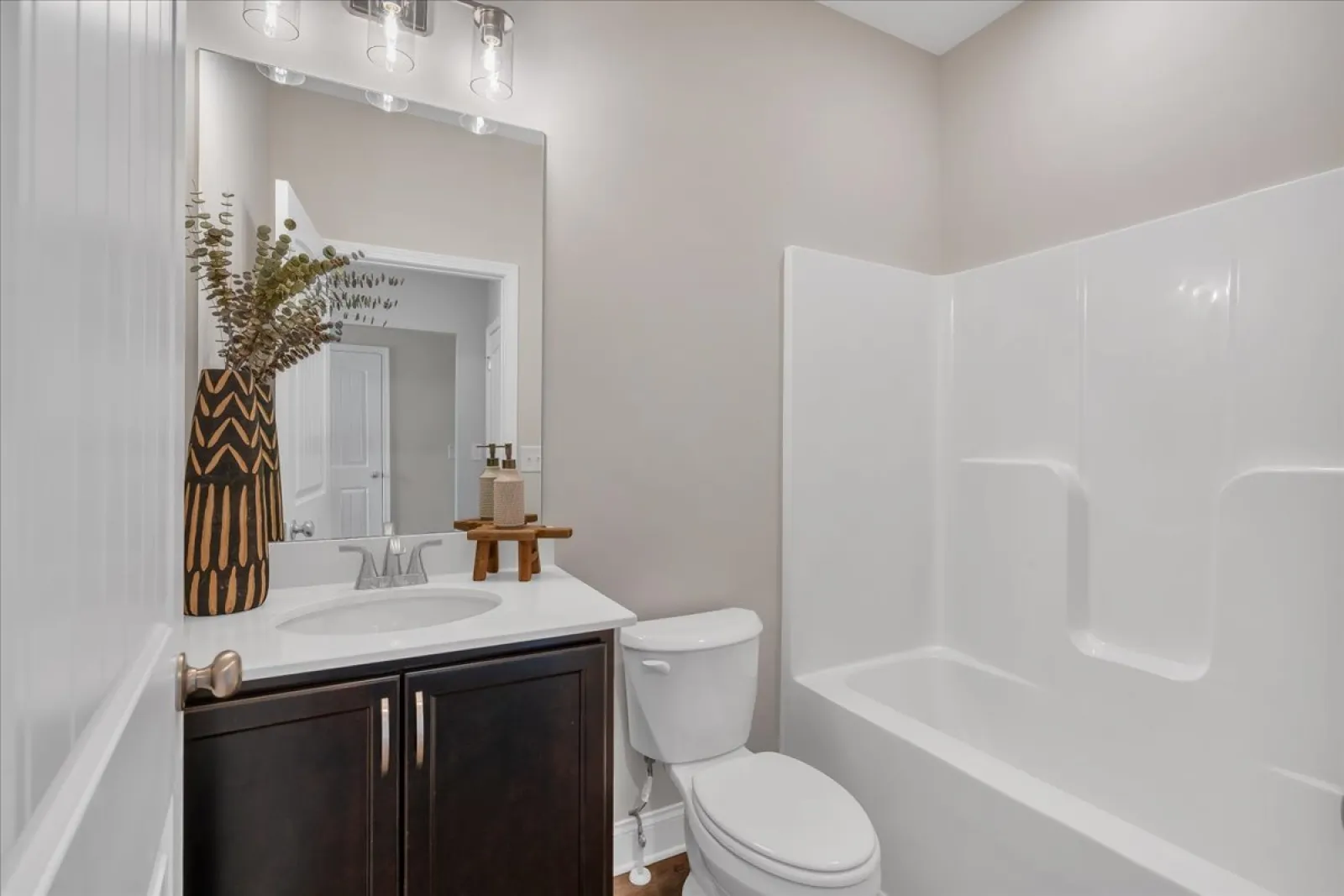 Modern bathroom with dark wood vanity, white countertop, toilet, and white bathtub with shower.