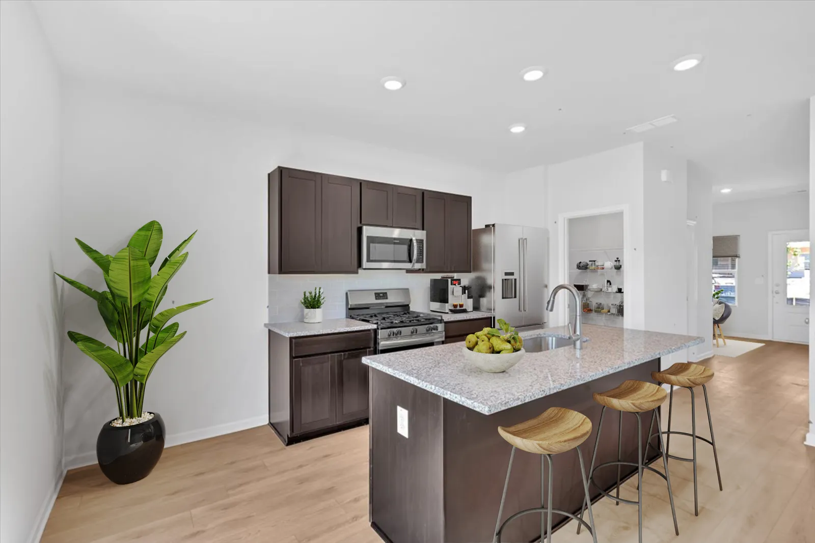 Modern kitchen with dark cabinets, granite island, stainless steel appliances, wooden stools, and a large green plant.