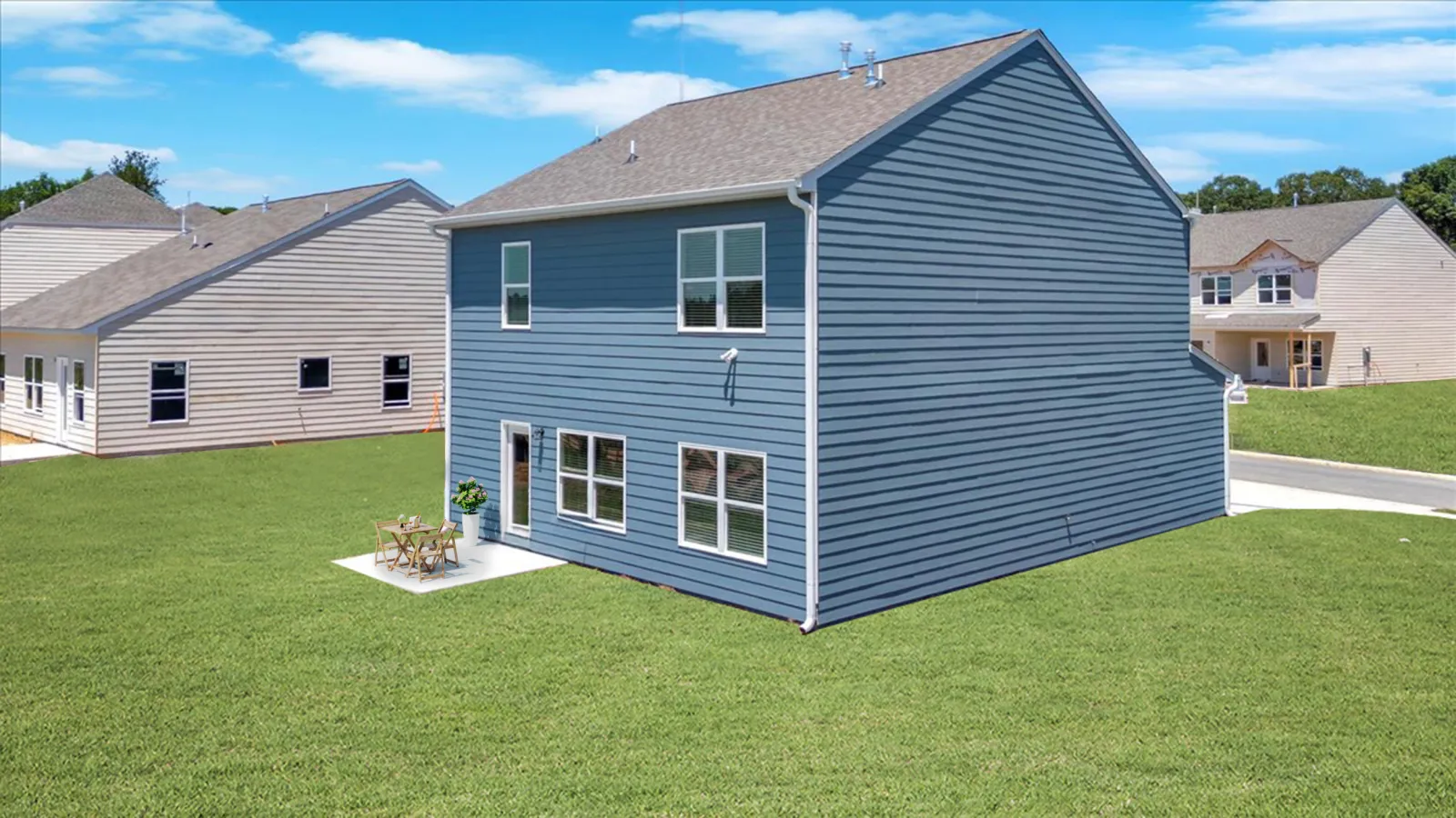 Blue two-story house with multiple windows and small patio on large green lawn under clear sky