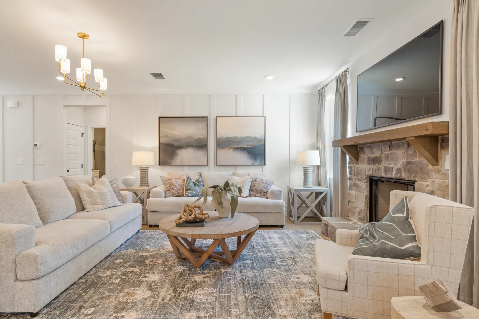 Bright living room with beige sofas, wooden coffee table, stone fireplace, abstract paintings, and modern lighting.