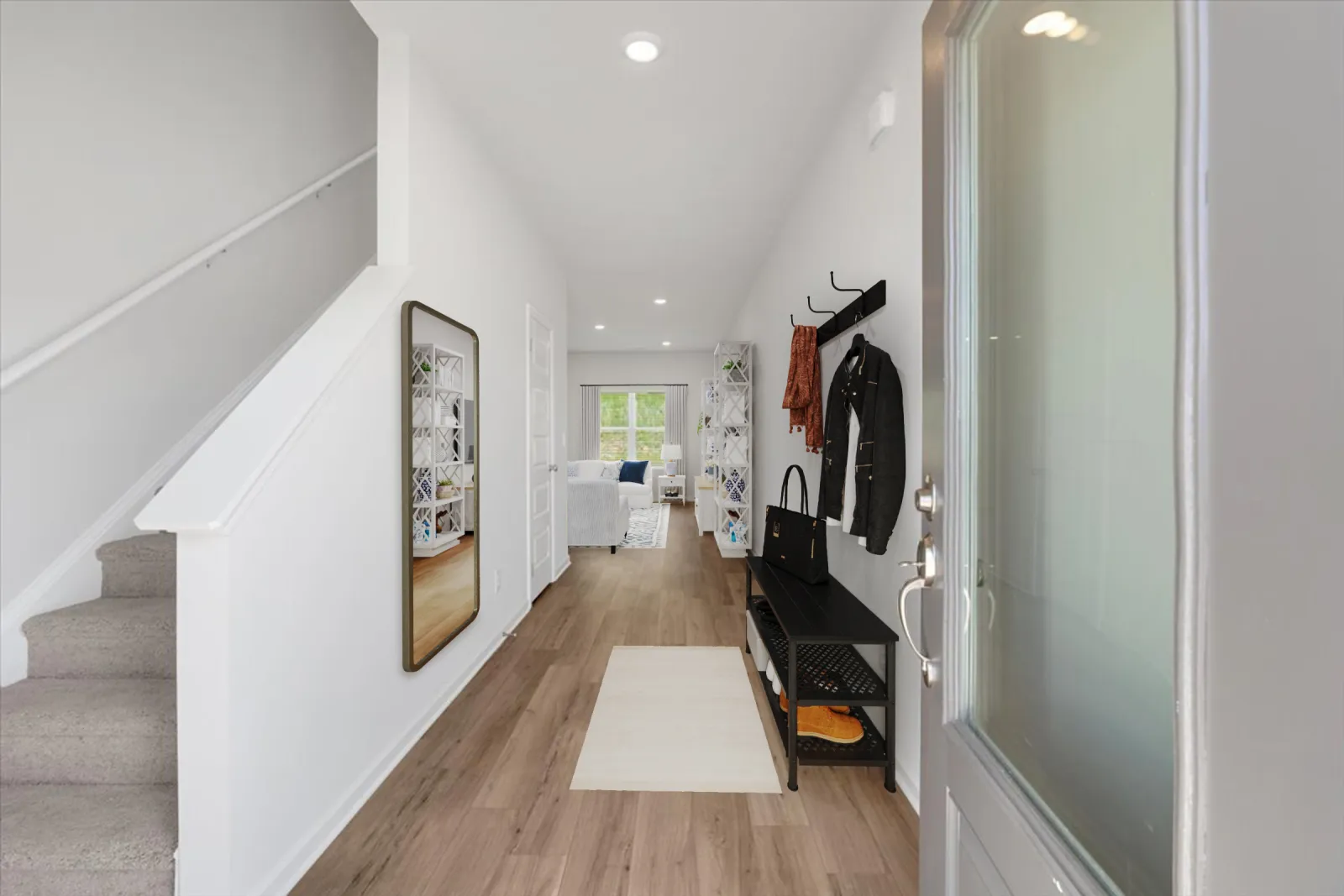 Bright entryway with wood flooring, staircase, mirror, coat rack, bench, and view into living room with large window.